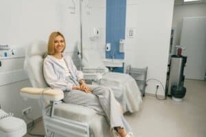 Smiling woman sitting in armchair while waiting for IV infusion during treatment in hospital