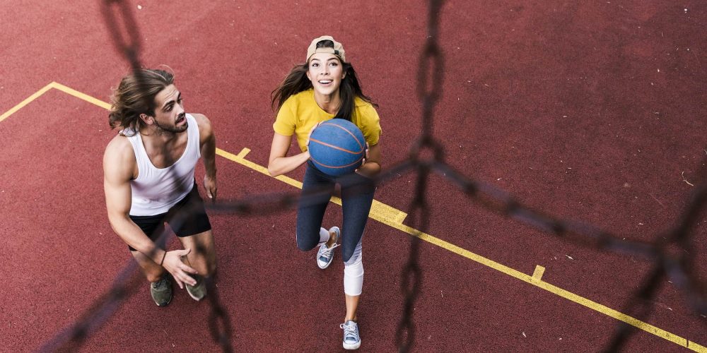 Young man and woman playing basketball on basketball ground